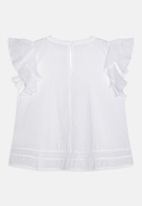 Blusa bianca in cotone con maniche corte a volant, scollatura rotonda e chiusura posteriore con bottoni. Il tessuto presenta un motivo a puntini.