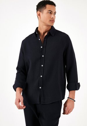Navy soft-textured shirt with a button-up front, long sleeves rolled at the cuffs, and a classic collar. Features white buttons.