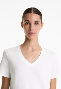 Tricou alb cu decolteu în V, fabricat dintr-un material moale și ușor. Mâneci scurte, croială lejeră, textură netedă, design minimalist. Fără modele sau accente.
