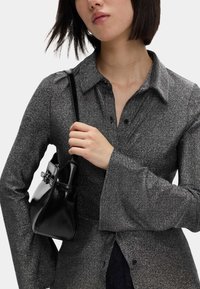 Glitrende grå langærmet skjorte med krave og flagrende ærmer. Sort læderhåndtaske med strop, som holdes i hånden, med en spænde detalje.