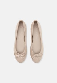 Ballerines en daim beige avec un bout arrondi, une doublure douce et un accent de nœud décoratif avec des pointes métalliques à l'avant.
