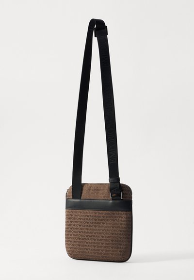Borsa a tracolla marrone con motivo a monogramma, dettagli neri lisci e una tracolla regolabile con logo in rilievo. Chiusura con zip superiore.