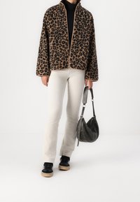 Leopardmönstrad jacka med dragkedja fram, parat med ljust ribbat byxor och svarta sneakers. Tillbehören inkluderar en grå axelväska.