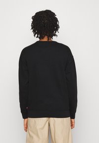 Sweat-shirt noir à col rond et manches longues. Tissu doux, coupe décontractée, avec poignets et ourlet côtelés. Aucun motif ni accent visible.