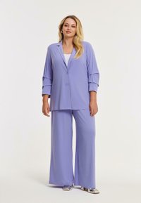 Lila twee-delige outfit met een knoopjesblazer met driekwart mouwen en brede pijpen. Glad materiaal met minimale accenten.
