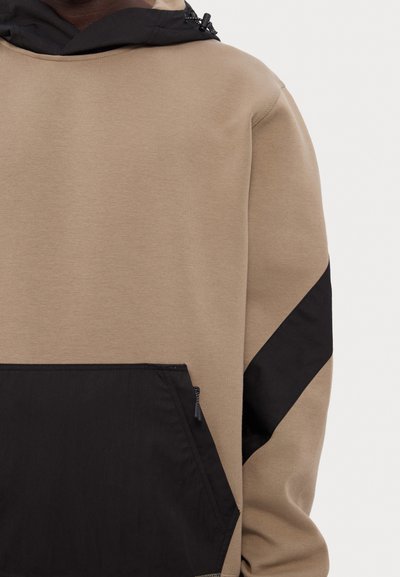 Felpa khaki con cappuccio nero e tasche, caratterizzata da un pannello diagonale nero e dettagli con zip. Tessuto morbido con una finitura a contrasto.