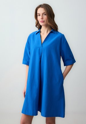 Robe bleue à manches courtes avec un col, de coupe évasée et poches latérales. Fabriquée dans un tissu léger au toucher doux.
