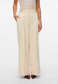 Pantalons larges en cream avec des plis à l'avant, des poches latérales et des accents à double bouton à la taille haute. Tissu lisse avec une texture douce.
