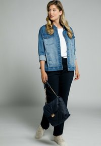 Chaqueta de mezclilla con cierre de botones y dos bolsillos en el pecho, combinada con una camiseta blanca y pantalones oscuros. Bolso acolchado en color marino y zapatillas color crema.