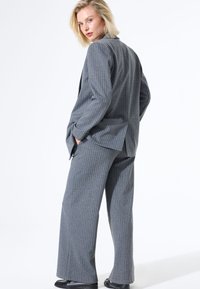 Blazer de rayas grises y pantalones de pierna ancha, con un ajuste entallado y textura suave. El material parece como lana con sutiles acentos en azul.