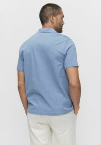 Ljusblå pikétröja med korta ärmar, gjord av mjukt tyg. Har en klassisk krage och en regular fit. Bärs med krämfärgade byxor.