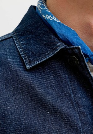 Primer plano del cuello de una chaqueta vaquera oscura con un pañuelo azul estampado alrededor del cuello en piel clara.