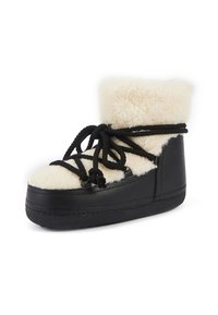 Bota de cuero negro con un puño de piel sintética color crema, con cordones negros y puntera redondeada. La suela es gruesa y plana para mayor estabilidad.