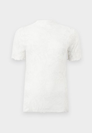 Valge lühikeste varrukatega top kõrge kaelusega ja keeruka lillelise pitsilise tekstuuriga kogu riidepinnal.