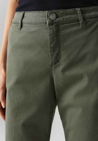Pantaloni verde oliva realizzati in un tessuto morbido. Presentano una chiusura con bottone, tasche frontali e un taglio dritto. Texture liscia con dettagli minimi.