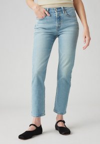 Lichtblauwe high-waisted jeans in een rechte pasvorm, gemaakt van denim met subtiele vervaging. Gecombineerd met zwarte platte schoenen met een kleine gesp.