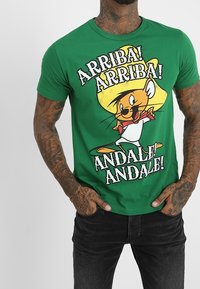 Zielona bawełniana koszulka z nadrukiem postaci z kreskówki w żółtym sombrero oraz tekstem "Arriba! Arriba! Andale! Andale!" napisanym dużymi czarnymi literami.