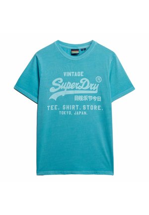 Turkise t-shirt lavet af blød bomuld, med et stort hvidt grafisk "SuperDry" logo med vintage stil tekst og detaljer.