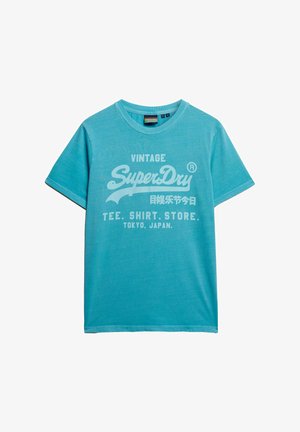 T-shirt turchese realizzato in morbido cotone, con un grande logo bianco "SuperDry" in stile vintage e dettagli decorativi.