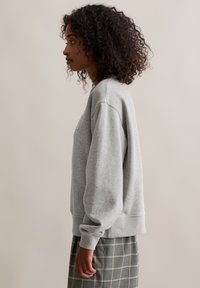 Grauer Pullover mit lässiger Passform, Rundhalsausschnitt und Bündchenärmeln, kombiniert mit einem gemusterten grünen Rock. Weiches Material.