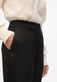 Pantaloni neri in tessuto testurizzato con un delicato motivo a rilievo. Design a vita alta con tasche laterali, abbinati a una blusa leggera.
