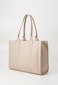 Borsa tote beige realizzata in tessuto testurizzato, dotata di due manici lunghi e un design strutturato con cuciture visibili e pannelli decorativi.