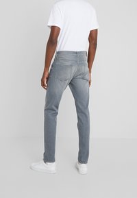 Los jeans de mezclilla gris presentan un ajuste recto y ajustado, un diseño de cinco bolsillos y un ligero desgaste. Se combinan con una camiseta blanca básica y zapatillas blancas.
