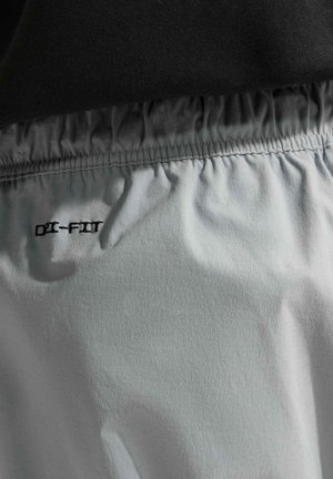 Elastyczny pas jasnoszarych spodenek Dri-FIT na czarnym tle, widok z bliska.