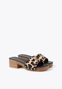 Sandalias de deslizamiento con estampado de leopardo, tira negra, acento de herrajes dorados y tacón de madera grueso. Textura suave con tachuelas doradas decorativas.