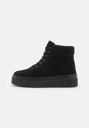 Black suede high-top sneakers with a plush inner lining, featuring a thick black platform sole and round laces through metal eyelets.