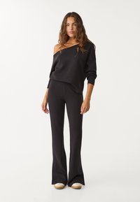Schwarzes Off-Shoulder-Sweatshirt kombiniert mit weit geschnittenen schwarzen Hosen. Beides aus weichem Material, mit lässigem Schnitt und minimalistischer Gestaltung.