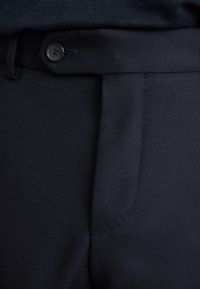 Pantalones ajustados azul marino con tejido texturizado, que cuentan con un cierre de botón y una cinturilla estructurada, además de bolsillos laterales.