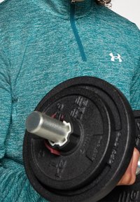 Turkos, långärmad, zip-up träningsskjorta med strukturfinish; håller en svart viktskiva med ett metallhandtag i mitten.