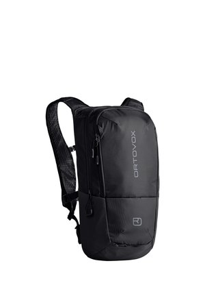 Mann mit beiger Jacke, schwarzem Fahrradhelm, Schutzbrille und schwarzem Rucksack mit Brustgurten, der leicht nach oben und seitlich schaut.