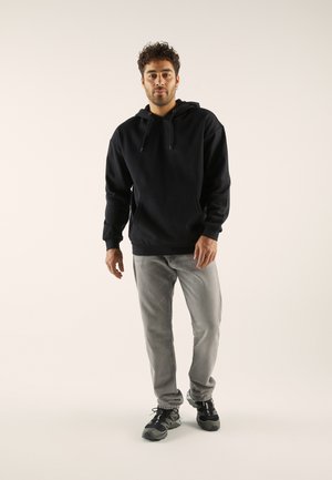 Felpa nera con tasca a marsupio e cappuccio con cordino, abbinata a jeans grigi e scarpe sportive nere. Design semplice, texture morbida.