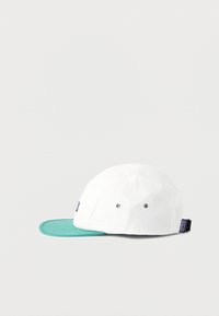 Λευκό καπέλο πέντε πάνελ με πράσινη επίπεδη γείσο, δύο μεταλλικές οπές αερισμού στο πλάι και μια μικρή μαύρη ετικέτα Patagonia στο πίσω μέρος.