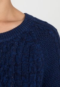 Dunkelblauer Strickpullover mit einem strukturierten Zopfmuster und einem gerippten Rundhalsausschnitt, der aus weicher, dicker Wolle gefertigt ist.