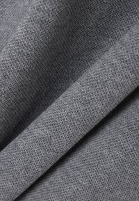 Szara dzianina o miękkiej fakturze i średniej grubości. Splot ukazuje delikatny wzór, tworząc subtelną głębię wizualną.