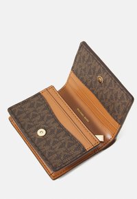 Portafoglio marrone Michael Kors aperto, che mostra gli scomparti per carte e la chiusura a bottone dorato con logo stampato all'interno.