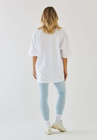 Overwymiarowy biały T-shirt, jasnoniebieskie legginsy, białe sneakersy i wzorzyste skarpetki. Gładka tkanina, luźny krój i swobodny design.