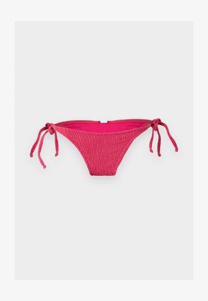 Bas de bikini rouge texturé avec cordons latéraux sur fond gris clair uni.