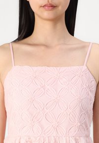 Ανοιχτό ροζ φόρεμα με λουλουδάτο κέντημα που περιλαμβάνει τρισδιάστατα λουλούδια και υφασμάτινες τιράντες, αναδεικνύοντας τις υφές και τα στρωμένα φρουφρού.