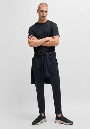 Svart idrottströja med korta ärmar, tillsammans med mörkblå joggers med en knytbar midja. Kompletteras med svarta sneakers.