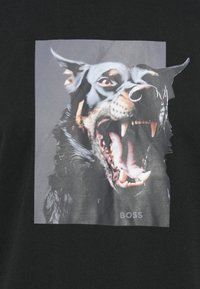 Črna majica s kratkimi rokavi z veliko grafiko režajočega psa, ki izpostavlja ostre zobe in izrazito teksturo dlake, z besedilom "BOSS" pod sliko.