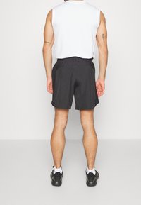 Svarta sportshorts med elastisk midja, sidofickor och lätt material, kombinerat med en ärmlös vit topp och svarta skor.