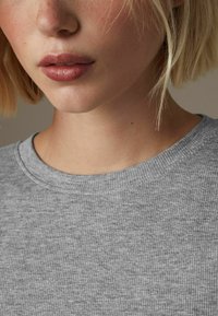 Pull gris côtelé avec un col rond. La texture est douce et le tissu semble léger et confortable. Aucun motif ou accent visible.