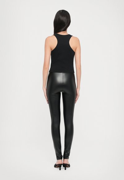 Must, ilma varrukat crop top ja kõrge vöökohaga mustad kunstnahast püksid. Sile tekstuur, sobiv siluett ja pahkluu pikkune disain.