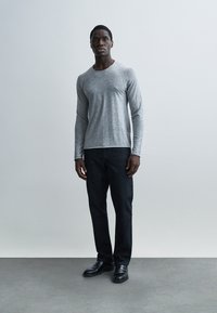 Γκρι πουκάμισο μακρυμάνικο συνδυασμένο με σκούρο τζιν και μαύρα παπούτσια. Το πουκάμισο έχει ομαλή υφή και στρογγυλεμένο λαιμόκοψη.