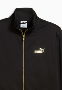 Giacca sportiva nera con colletto alto, zip dorata e logo PUMA in oro. Tessuto morbido con una texture liscia.