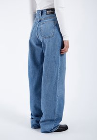 Light blue denim jeans with a loose fit, high waist, and sturdy stitching. Features two back pockets and a black label at the waistband.